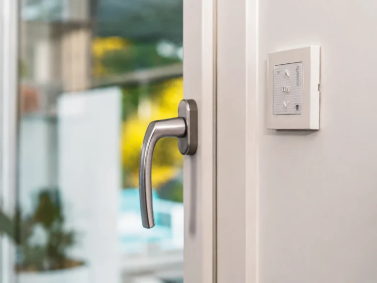 Detail moderního ovládacího panelu Somfy vedle dveřní kliky – elegantní řešení pro chytré řízení stínicí techniky a komfortní ovládání pergol či rolet.